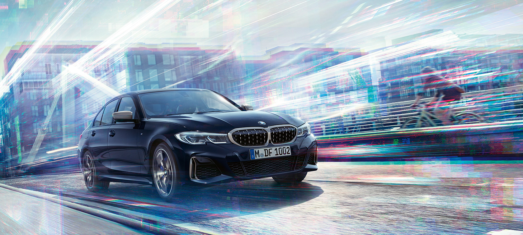 BMW Serije 3 Sedan, BMW M340i xDrive. Tročetvrtinski bočni pogled na BMW M340i xDrive koji vozi putem spram urbane pozadine.