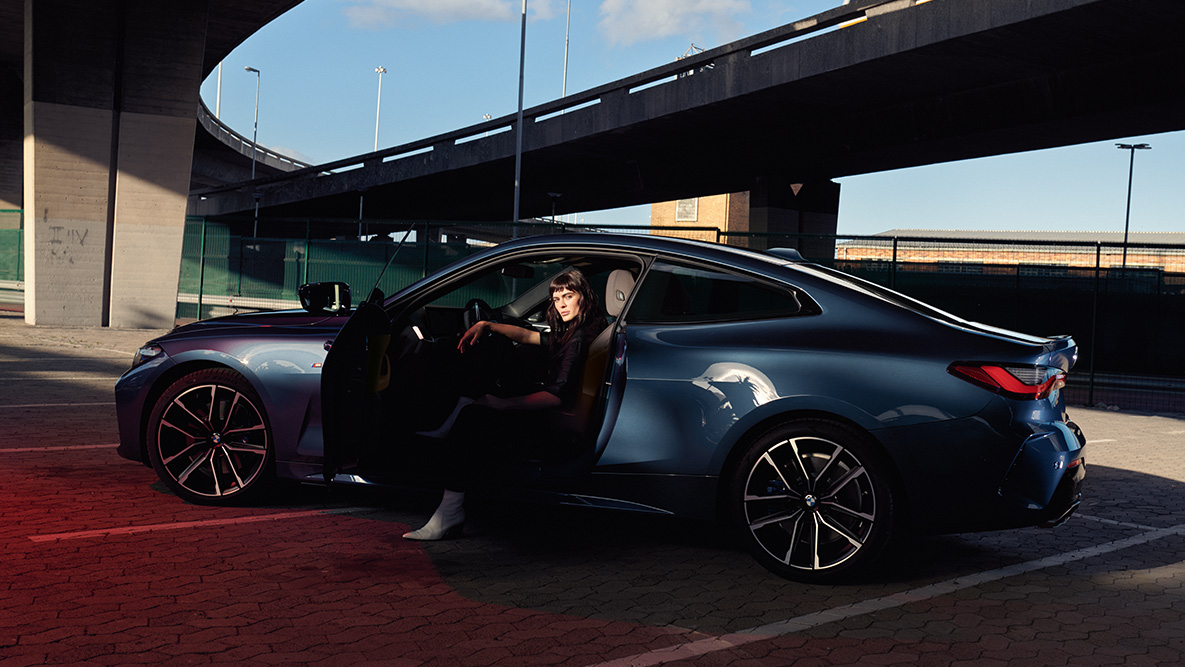 Bočni prikaz točkova od lakih legura BMW Serija 4 Coupe G22 2020 BMW Serija 4 Coupe G22 2020 Arctic Race plava metalizirana boja bočni prikaz točkova od lakih legura i modela u vozilu s otvorenim vratima