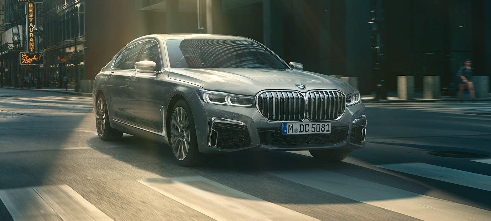 BMW Serija 7 Limuzina G11/G12 2019 Bernina siva boja s efektom ćilibara, tročetvrtinski prednji prikaz vozila u pokretu BMW Serija 7 Limuzina G11 G12 2019 Bernina siva boja s efektom ćilibara, tročetvrtinski prikaz prednje strane vozila tokom vožnje u urbanom okruženju