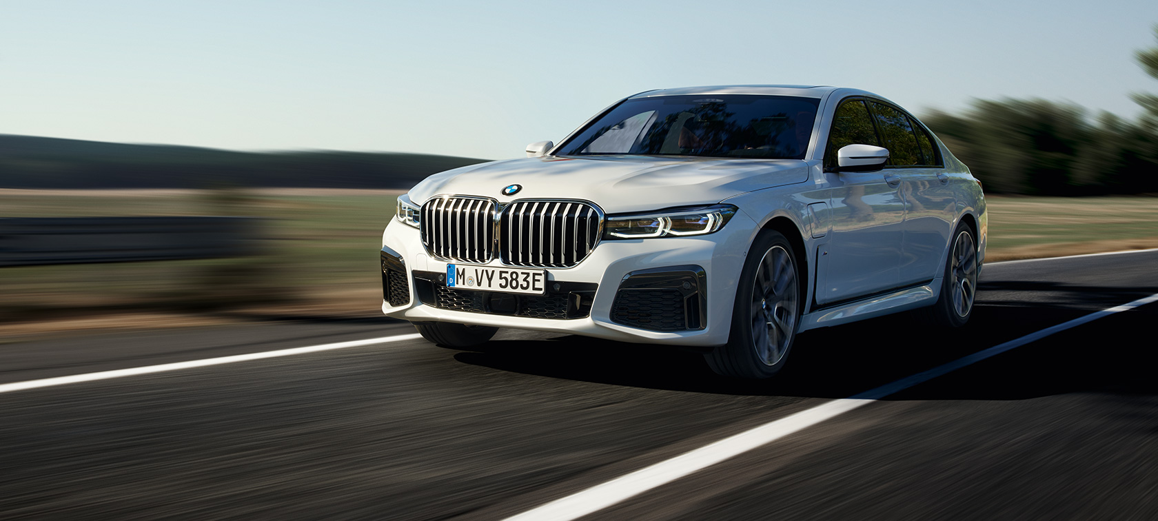 BMW 745e Limuzina plug-in hibrid G11 G12 Mineral bela metalik boja tročetvrtinski prednji prikaz BMW 745e Limuzina plug-in hibrid G11 G12 Mineral bela metalik boja tročetvrtinski prednji prikaz tokom vožnje preko seoskog puta