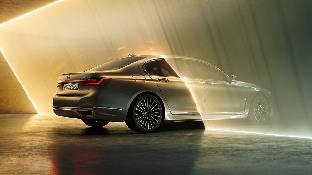 BMW Serija 7 Limuzina G11 G12 2019 Bernina siva BMW Serija 7 Limuzina G11 G12 2019 Bernina siva boja s efektom ćilibara, tročetvrtinski stražnji prikaz vozila okružen snopom svetla