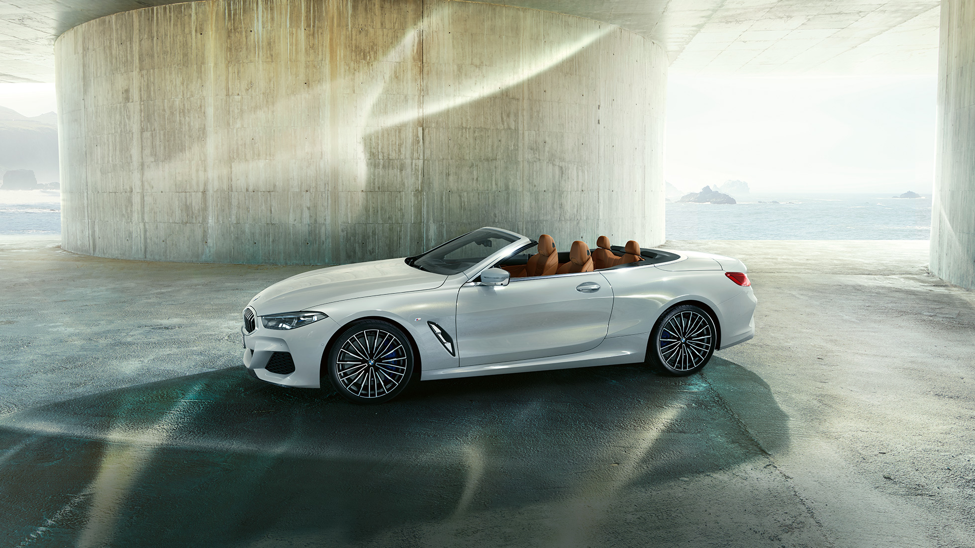 BMW M850i xDrive u boji Mineral White metaliziranoj, pogled sa strane s otvorenim mekim krovom. BMW M850i xDrive u boji Mineral White metaliziranoj, pogled sa strane s otvorenim mekim krovom.