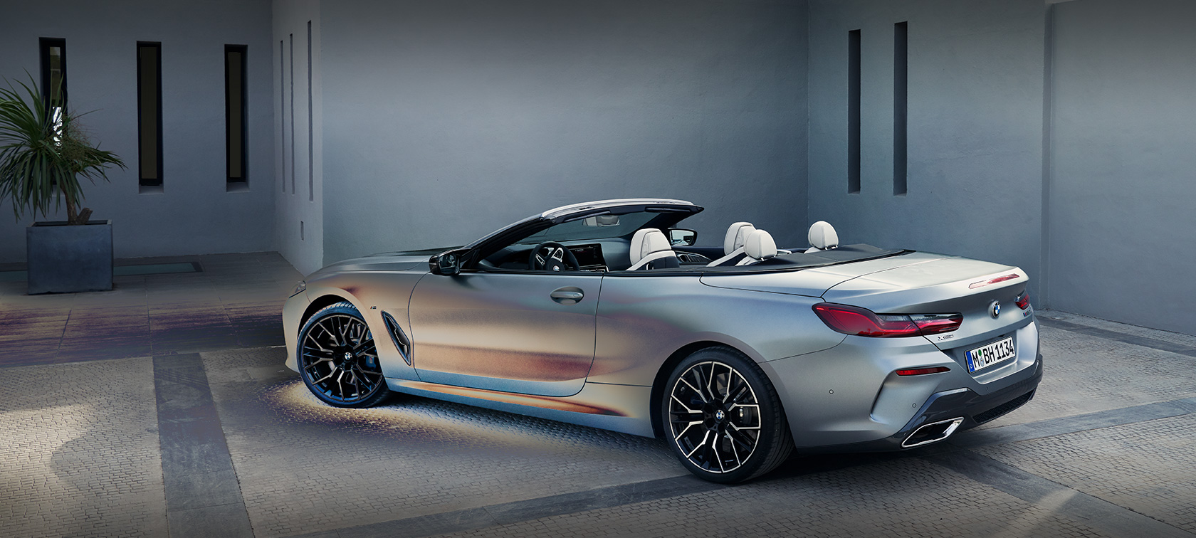 Čovek naslonjen na BMW-u Serije 8 Cabrio G14 LCI Facelift 2022 BMW Individual Frozen Pure sive metalik boje bočni prikaz parkiranog vozila ispred zgrade sa muškim modelom