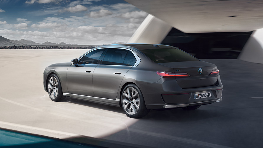 BMW i7 Sedan paket 3/4 zadnji prikaz BMW i7 Sedan G70 BMW Individual Oxid siva metalik boja tročetvrtinski zadnji prikaz vozila parkiranog ispred zgrade