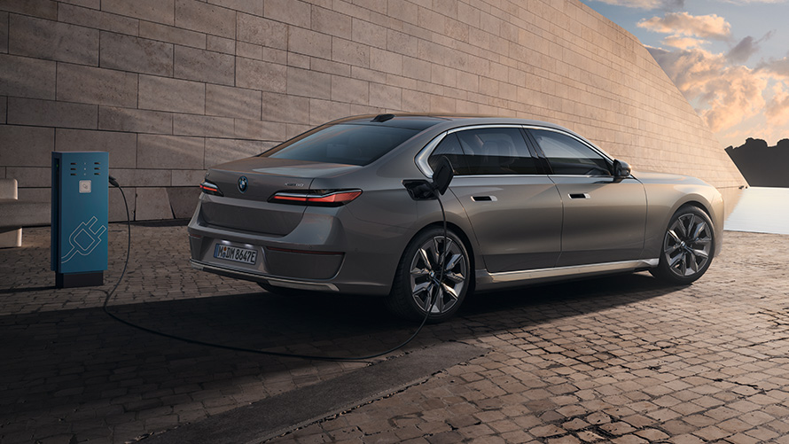 BMW i7 Sedan G70 3/4 bočni prikaz zadnjeg dela vozila BMW i7 Sedan G70 BMW Individual Oxid siva metalik boja tročetvrtinski bočni prikaz zadnjeg dela vozila na stanici za punjenje