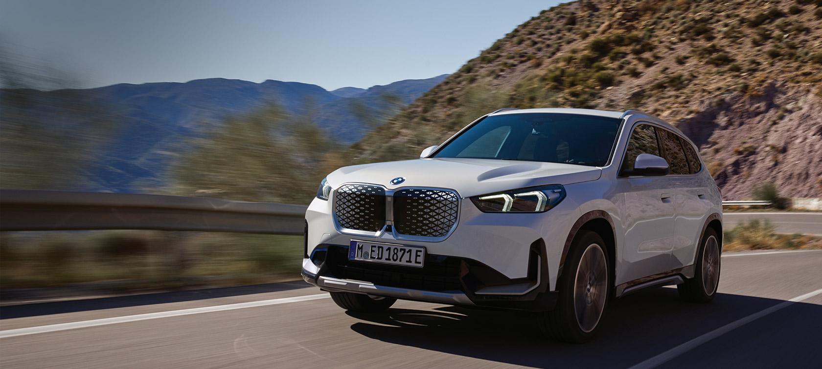 BMW iX1 U11 BEV 2022 Mineral bela metalik boja tročetvrtinski prednji prikaz vozila tokom vožnje krivudavim planinskim putem