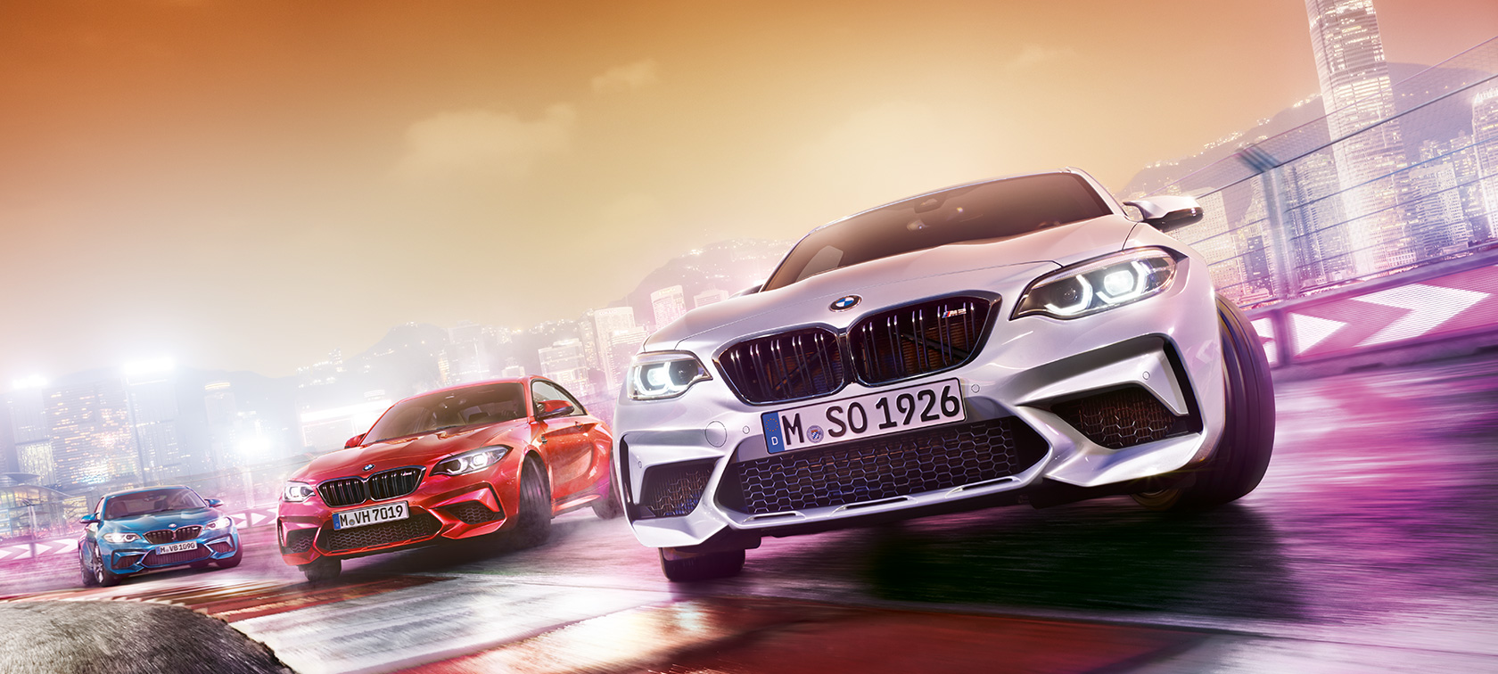BMW M2 Competition u akciji Tri modela BMW M2 Competition klize po trkačkoj stazi ispred noćnog gradskog pejzaža.