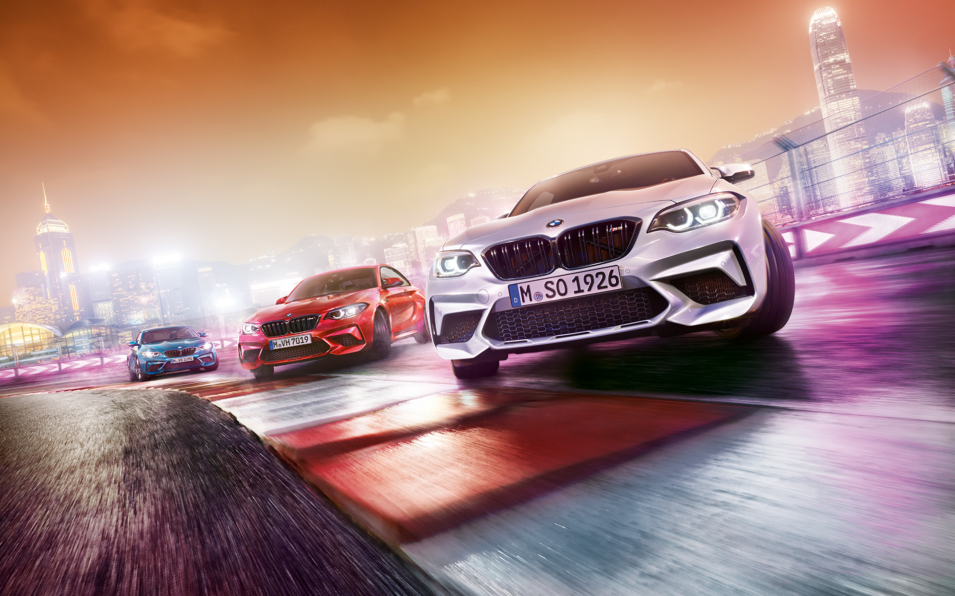 BMW M2 Competition u akciji Tri modela BMW M2 Competition klize po trkačkoj stazi ispred noćnog gradskog pejzaža.