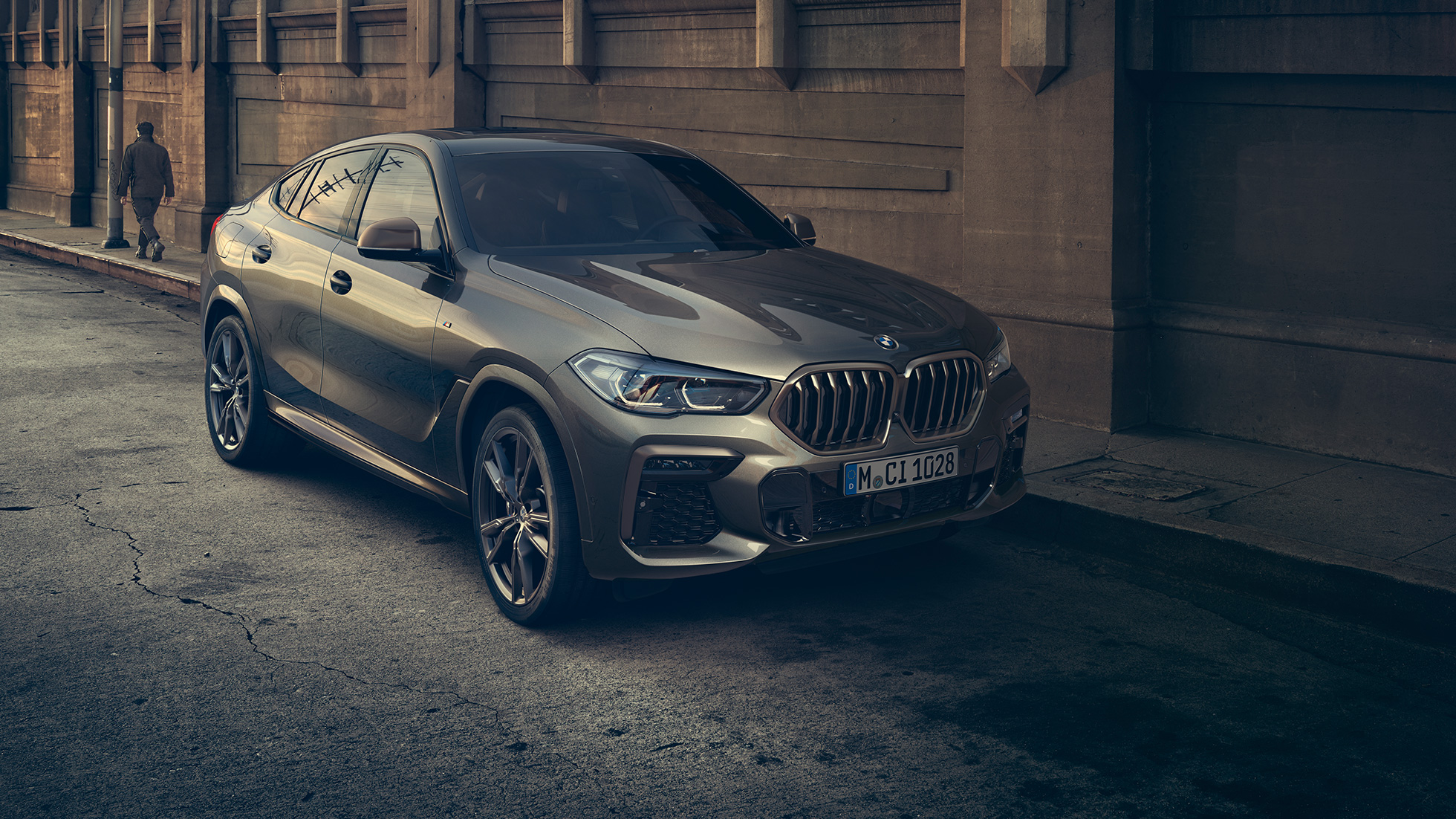 BMW X6 M50i stoji. BMW X6 M50i u tročetvrtinskoj perspektivi spreda stoji ispred urbanog prizora.
