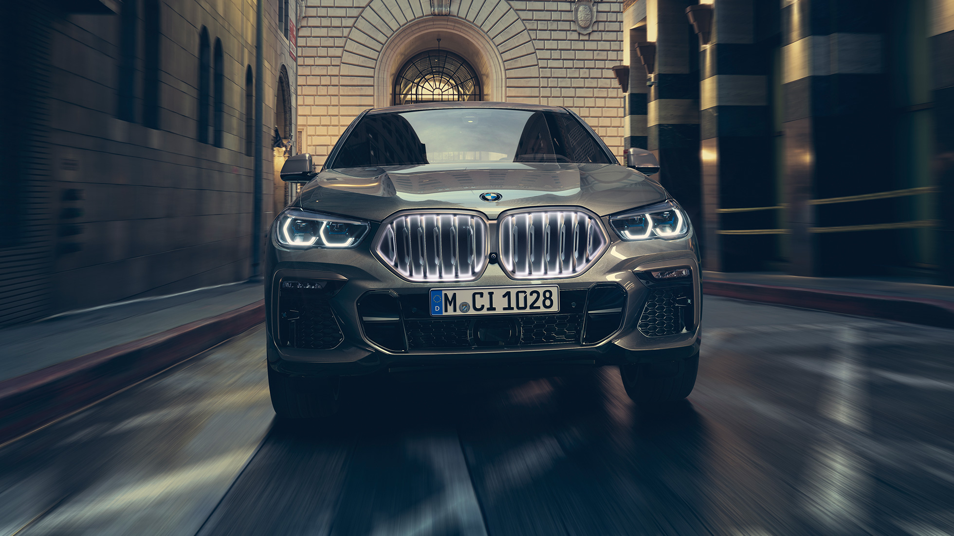 BMW X6 M50i sa BMW prednjom rešetkom „Iconic Glow“. BMW X6 M50i u prednjoj perspektivi ispred urbanog prizora.