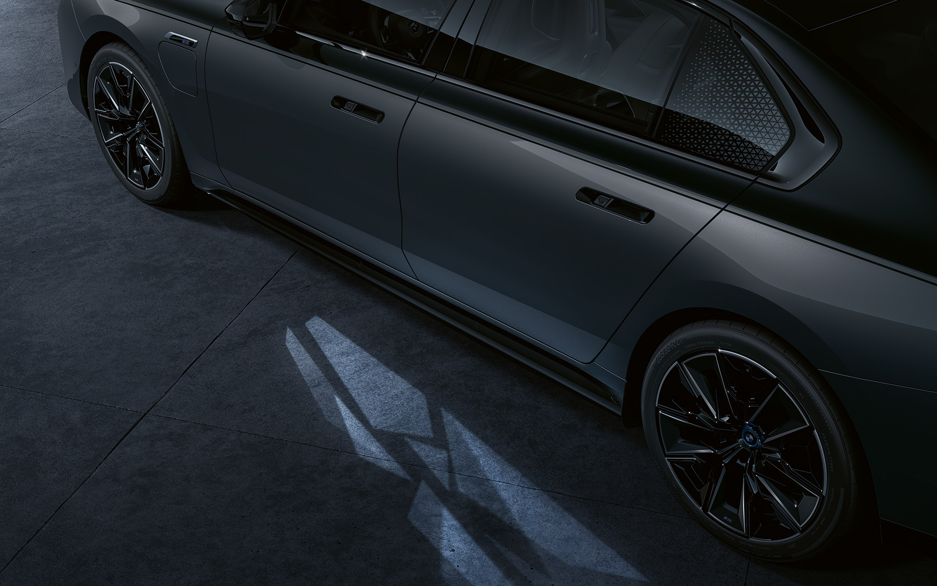 Koncept osvetljenja BMW M760e xDrive Sedan G70 BMW Individual dvonijansna Black Sapphire metalik boja karoserije BMW Individual Dravite siva metalik boja bliži bočni prikaz s uključenim Welcome Light Carpet