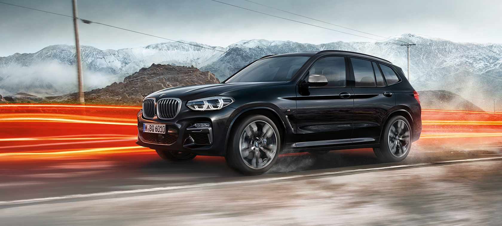BMW X3 M40i i BMW X3 M40d, pogled sa strane. BMW X3 M40i i BMW X3 M40d u boji Black Sapphire metaliziranoj, u vožnji, eksterijer, pogled sa strane ispred planinskog pejzaža sa svetlosnim prugama.