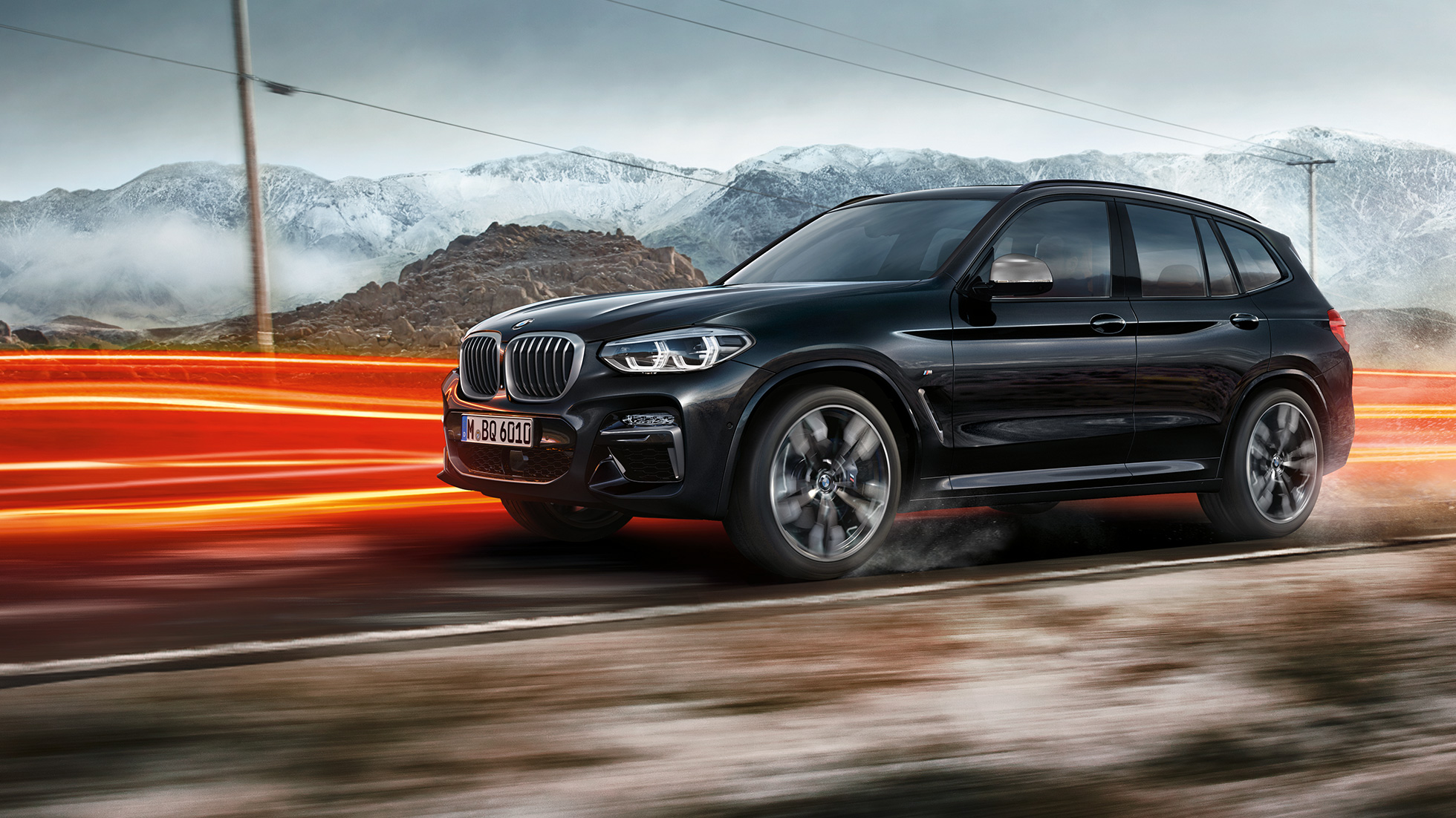 BMW X3 M40i i BMW X3 M40d, pogled sa strane BMW X3 M40i i BMW X3 M40d u boji Black Sapphire metaliziranoj, u vožnji, eksterijer, bočni pogled ispred planinskog pejzaža sa svetlčim prugama.