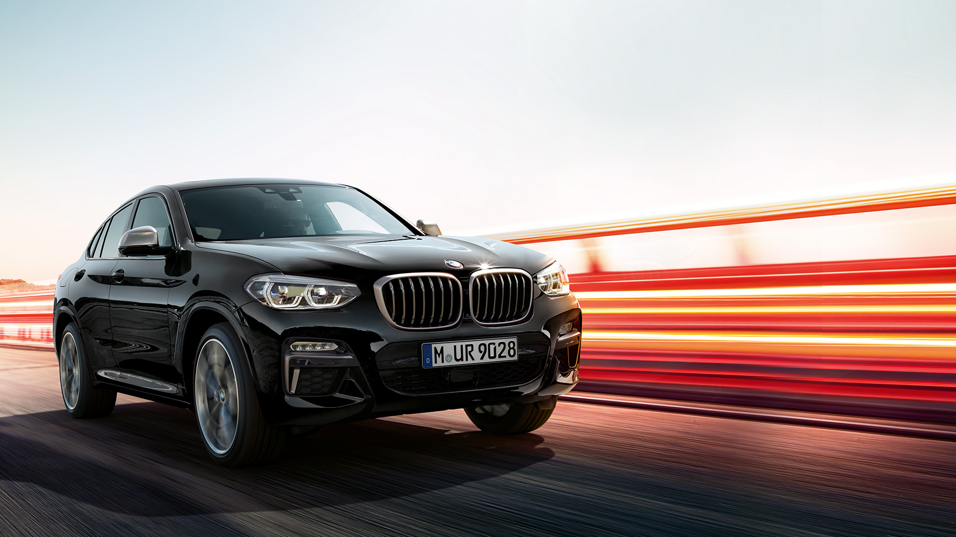 BMW X4 M40i, tročetvrtinski pogled otpozadi. BMW X4 M40i u boji Black Sapphire metaliziranoj, u vožnji, eksterijer, tročetvretinski pogled otpozadi sa svetlosnim prugama.