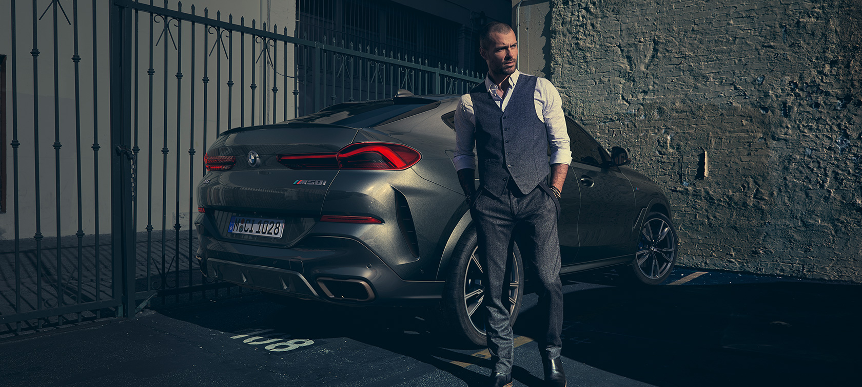 BMW X6 M50i tročetvrtinski zadnji prikaz G06 Čovek stoji pored modela BMW X6 M50i G06 2018 SUV tročetvrtinski prikaz otpozadi