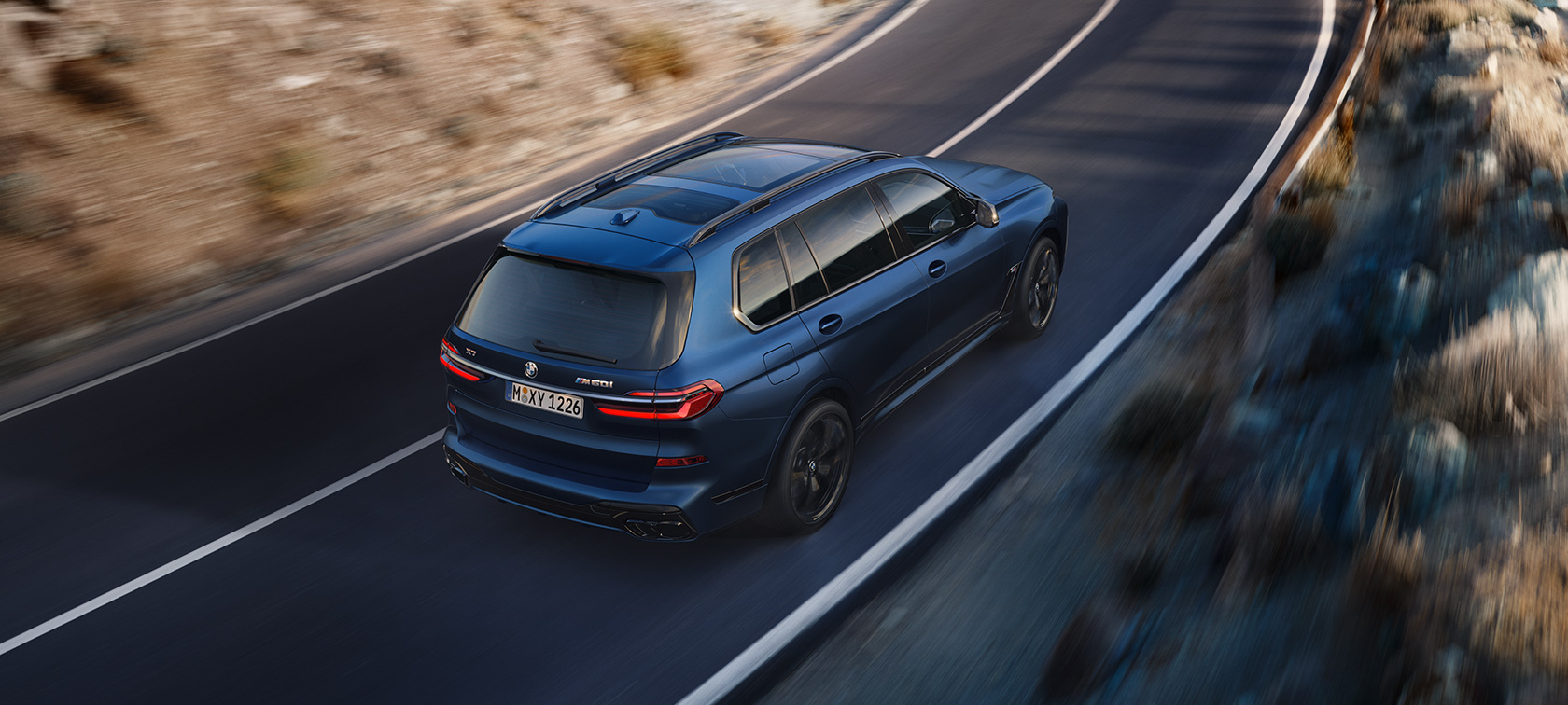 BWM X7 M60i xDrive G07 LCI Frozen Marina Bay plave boje tročetvrtinski zadnji prikaz vozila iz ptičije perspektive tokom vožnje ulicom