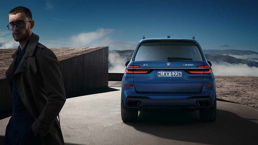 BWM X7 M60i xDrive G07 LCI Frozen Marina Bay plave boje prikaz zadnjeg dela parkiranog vozila s planinskom pejsažom u pozadini BWM X7 M60i xDrive G07 LCI Frozen Marina Bay plave boje prikaz zadnjeg dela parkiranog vozila s planinskim pejsažom u pozadini i modelom