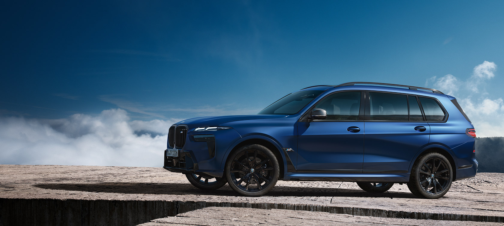 BWM X7 M60i xDrive G07 LCI Frozen Marina Bay plave boje bočni prikaz parkiranog vozila s planinskim pejsažom u pozadini