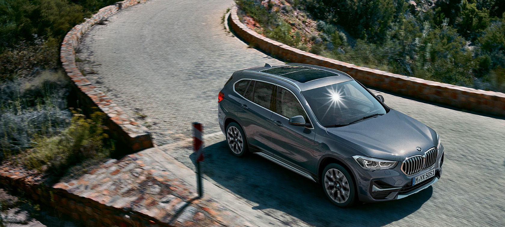 BMW X1, tročetvrtinski pogled spreda. BMW X1, tročetvrtinski pogled spreda u vožnji ispred planinskog pejzaža.