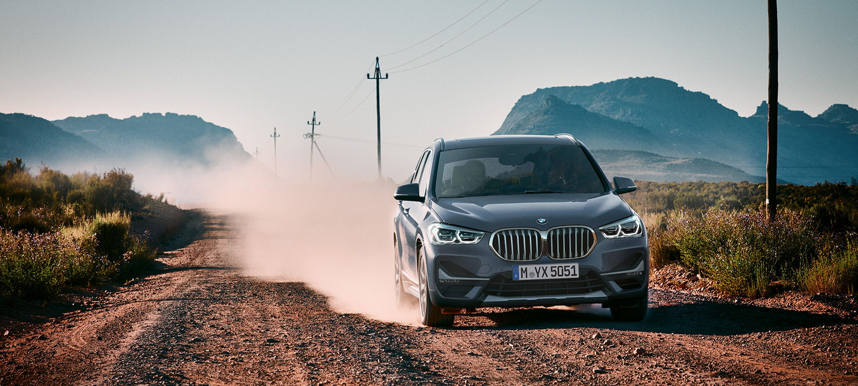BMW X1, tročetvretinski pogled otpozadi. BMW X1, tročetvrtinski pogled otpozadi u vožnji ispred planinskog pejzaža.