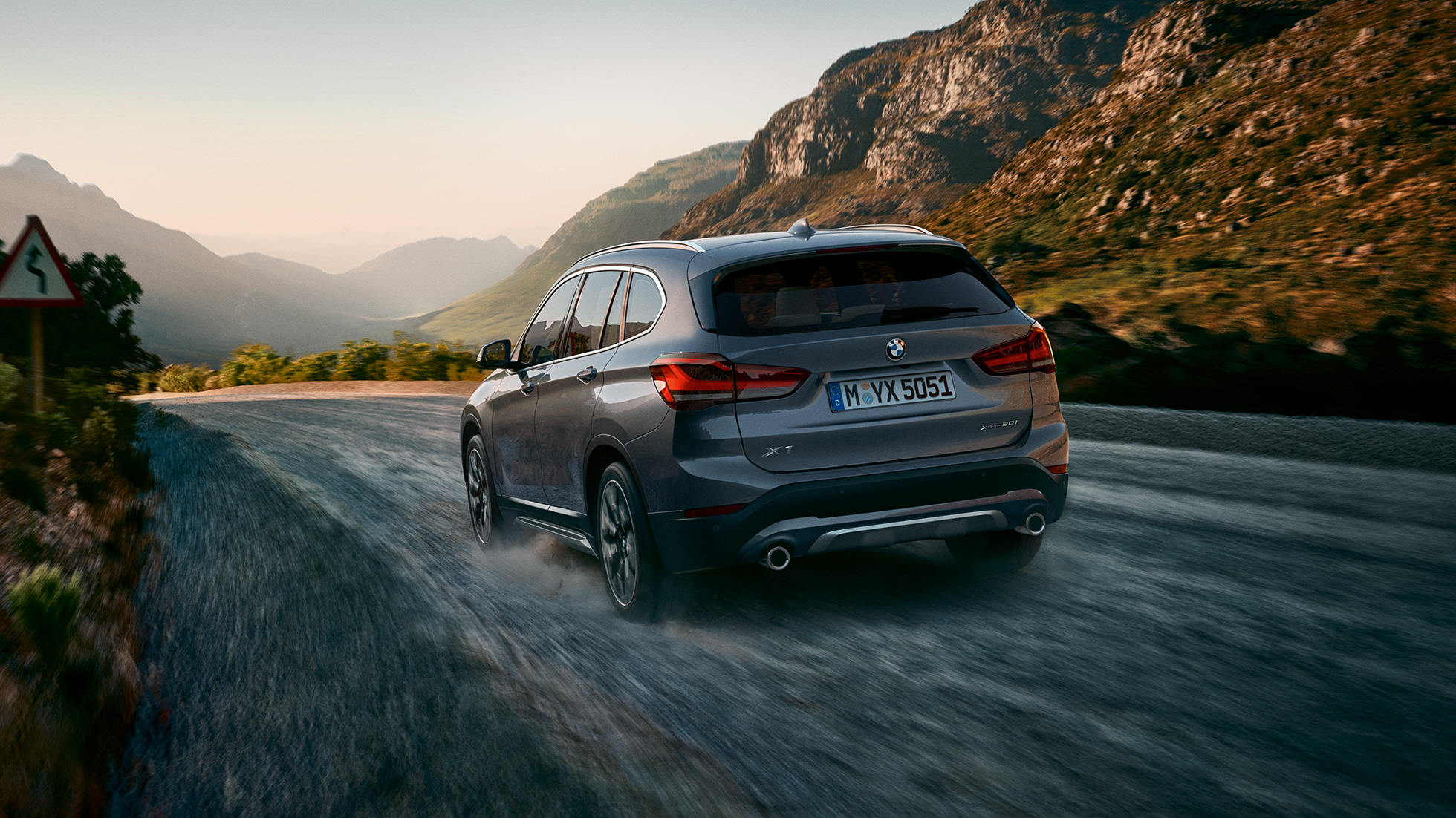 BMW X1, tročetvrtinski pogled otpozadi. BMW X1, tročetvrtinski pogled otpozadi u vožnji ispred planinskog pejzaža.