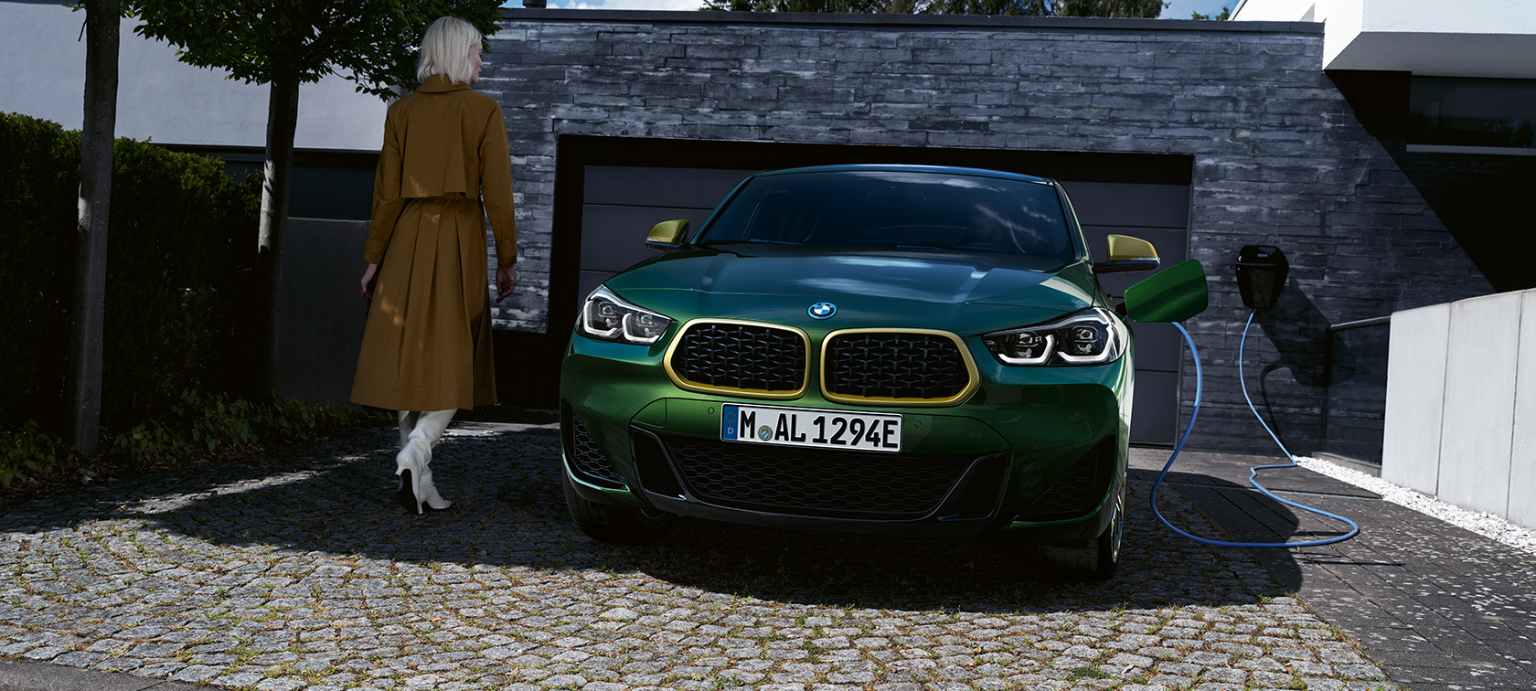 Prednji prikaz BMW-a X2 F39 Sanremo zelene metalik boje Prednji prikaz vozila tokom napajanje sa modelom na levoj strani BMW-a X2 F39 Sanremo zelene metalik boje