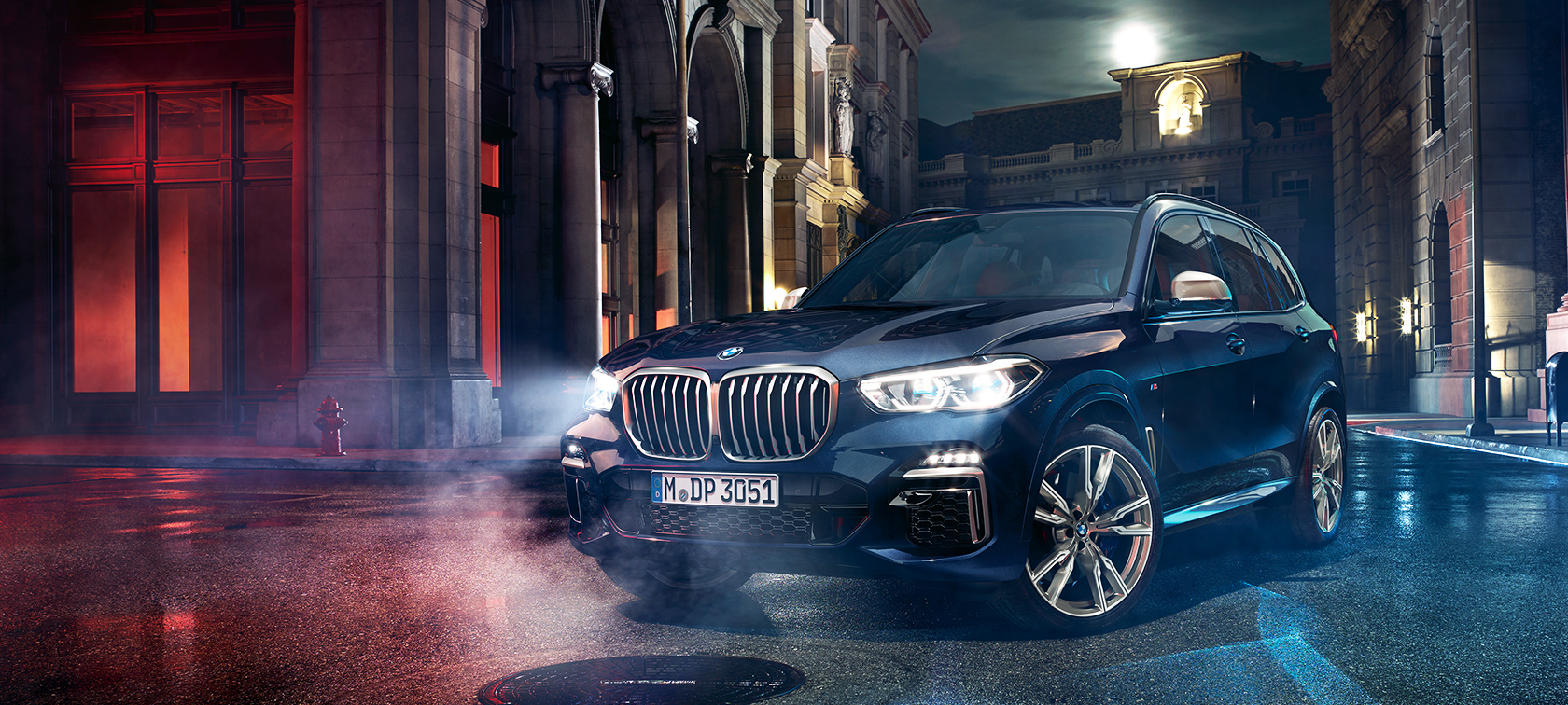 BMW X5 M50d na putu BMW X5 M50d stoji na putu noću spram gradskog pejzaža