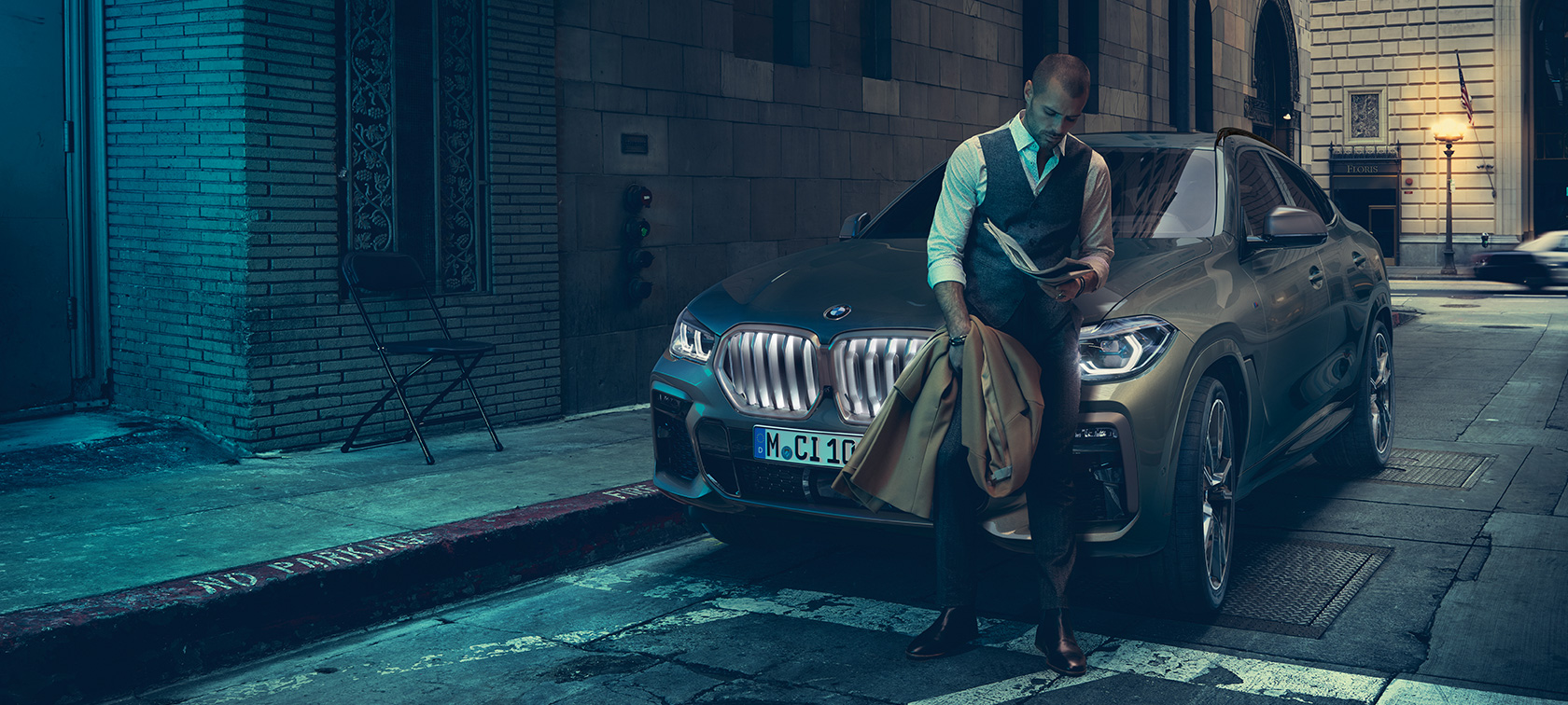 Čovek naslonjen na BMW X6. Čovek naslonjen na BMW X6 u bočnoj perspektivi ispred urbanog prizora.