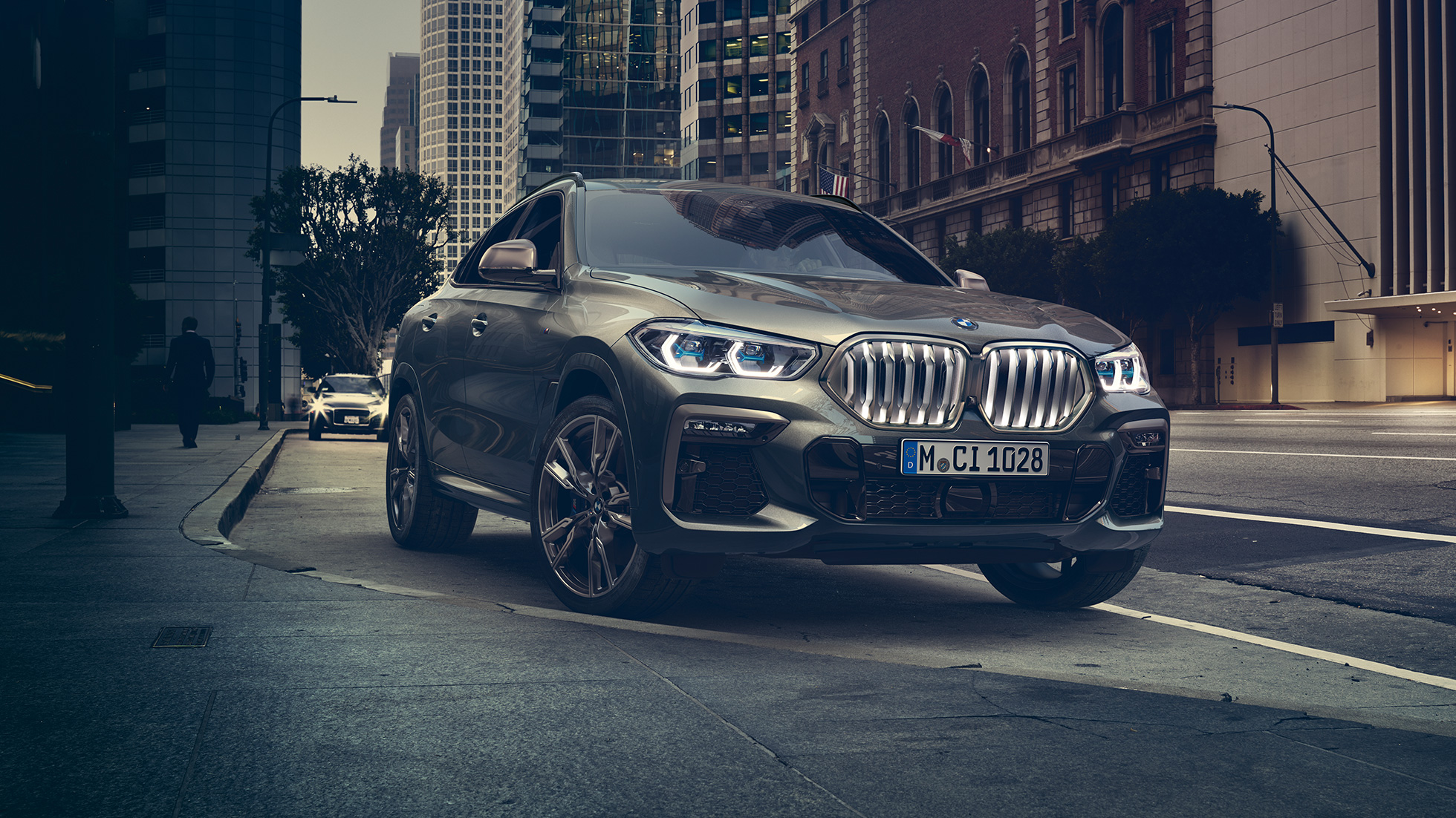 BMW X6 Adaptivno M ogibljenje Professional BMW X6 u tročetvrtinskom pogledu spreda ispred urbanog prizora.