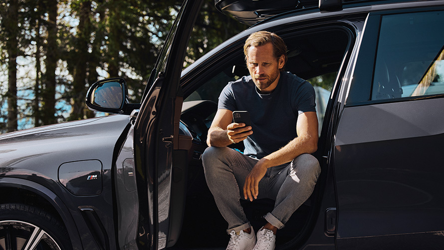 Čovek koji sedi u BMW-u i gleda svoj telefon BMW prolećni letnji dodaci Čovek koji sedi u BMW-u i gleda svoj telefon